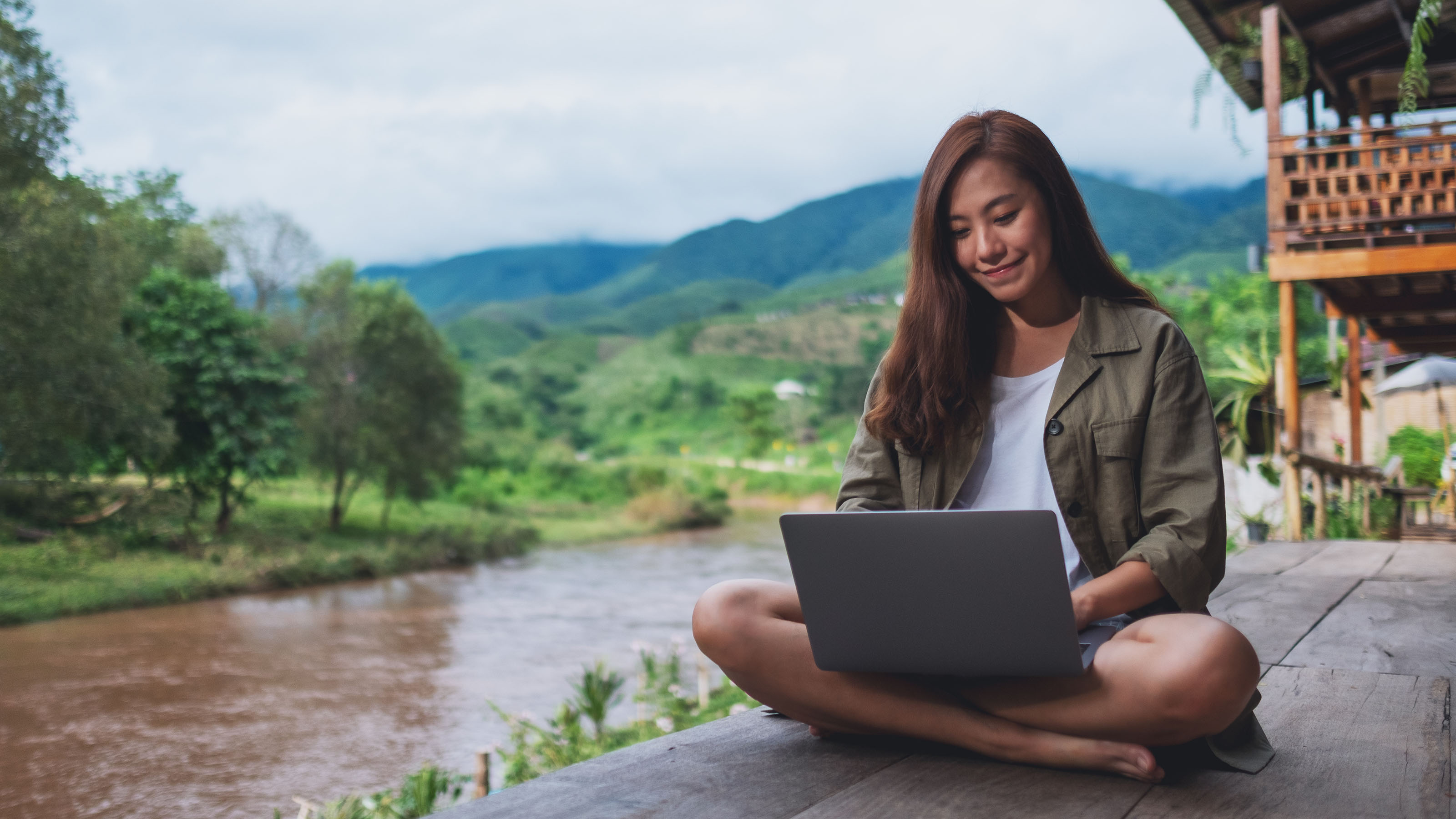 Une travailleuse des TI avec son ordinateur portable sur le bord d'une rivière.